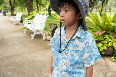 Téléchargez les photos : Heureux asiatique préscolaire garçon marche dans vert tropical arbre forêt dans ville parc loisirs de plein air - en image libre de droit