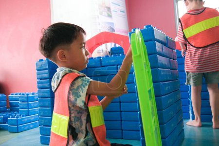 Téléchargez les photos : Jardin d'enfants asiatique garçon jouer ingénieur construction mécanique homme carrière bloc de couleur bâtiment aire de jeux intérieure - en image libre de droit