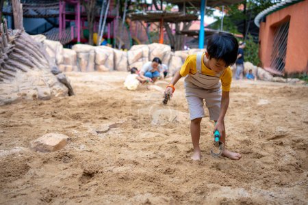 Téléchargez les photos : Asiatique enfant garçon 5 ans profiter de jouer bac à sable en plein air avoir du plaisir sur aire de jeux dans le bac à sable. Activités créatives de jardin d'enfants en plein air - en image libre de droit