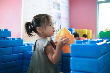 Foto de Adorable niña disfrutando con la construcción de bloques de juguete patio interior feliz niña preescolar - Imagen libre de derechos