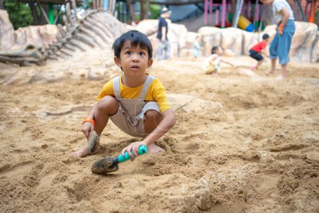 Photo for Asian kindergarten 5 year old playing in sandbox having fun on playground in sandpit. Outdoor creative activities - Royalty Free Image