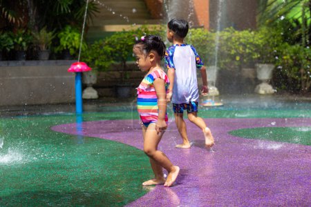 Foto de Feliz niño y niña disfrutando de salpicaduras de agua al aire libre parque acuático vacaciones de verano - Imagen libre de derechos