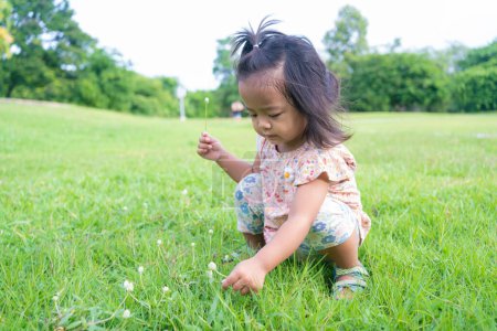 Photo for Adorable little child girl playing on green meadow grass outdoor city park happy asian girl - Royalty Free Image