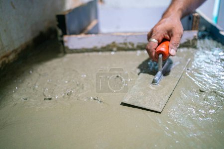 Téléchargez les photos : Homme mécanique plaçant à la main ciment plancher intérieur maison de construction rénover - en image libre de droit