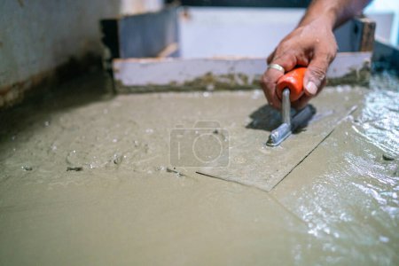 Téléchargez les photos : Homme mécanique plaçant à la main ciment plancher intérieur maison de construction rénover - en image libre de droit