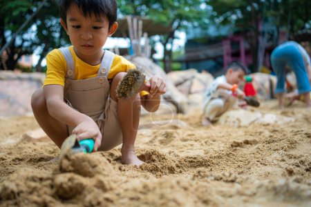 Foto de Asiático niño de 5 años disfrutando de jugar al aire libre sandbox divertirse en el patio de recreo en arenero. Actividades de jardín de infancia creativo al aire libre - Imagen libre de derechos