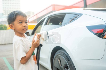 Téléchargez les photos : Petit garçon utiliser EV charge de voiture sur la station de voiture électrique voyage de vacances éco transport vert - en image libre de droit