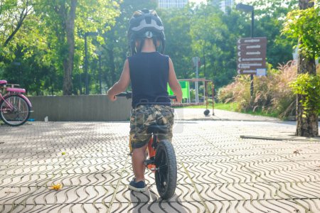 Téléchargez les photos : Préscolaire asiatique garçon pratique équitation balansc vélo dans ville parc activité de plein air - en image libre de droit