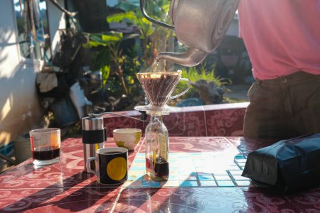 Téléchargez les photos : Homme drrip main brassage café local par du papier filtré sur la table matin en plein air à la maison - en image libre de droit