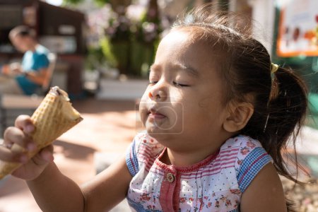Foto de Feliz asiático preescolar chica disfrutando comer helado viaje en verano ciudad - Imagen libre de derechos