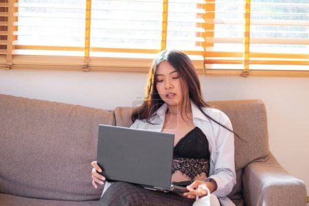 Téléchargez les photos : Business asiatique casual femme dactylographier sur ordinateur portable assis sur canapé dans confortable bureau à domicile technologie de l'information - en image libre de droit