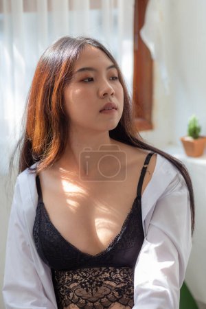 Téléchargez les photos : Belle asiatique 20s sexy femme dans confortable chambre avec fenêtre et rideau en noir sous-vêtements portrait femme - en image libre de droit