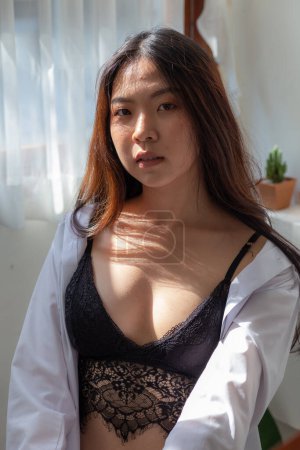 Foto de Hermosa asiático 20s sexy mujer en acogedor habitación con ventana y cortina en negro ropa interior retrato mujer - Imagen libre de derechos