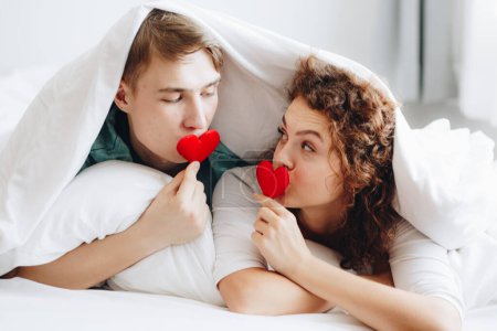 Téléchargez les photos : Couple d'amour couché sur une couverture de lit blanche tenir coeur symbole concept valentine - en image libre de droit