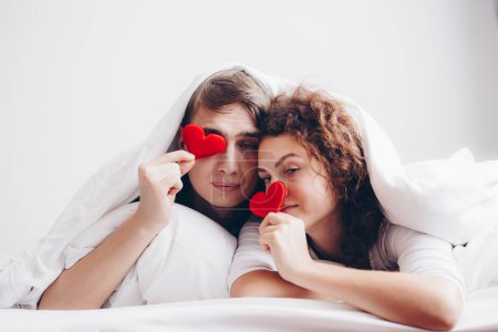 Photo for Love couple lying on white bed blanket hold heart symbol valentine concept - Royalty Free Image