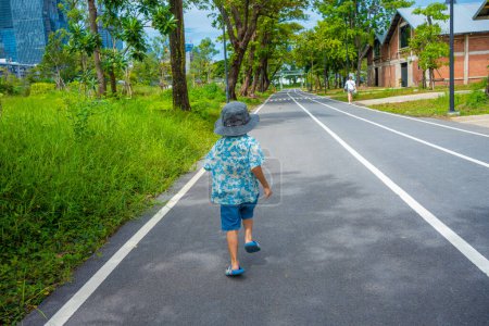 Téléchargez les photos : Petit garçon marchant sur le sentier du parc municipal forêt d'arbres verts loisirs de plein air - en image libre de droit