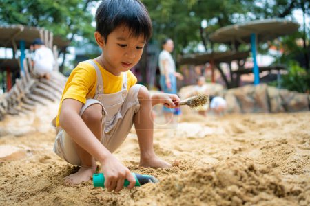 Foto de Asiático niño de 5 años disfrutando de jugar al aire libre sandbox divertirse en el patio de recreo en arenero. Actividades de jardín de infancia creativo al aire libre - Imagen libre de derechos