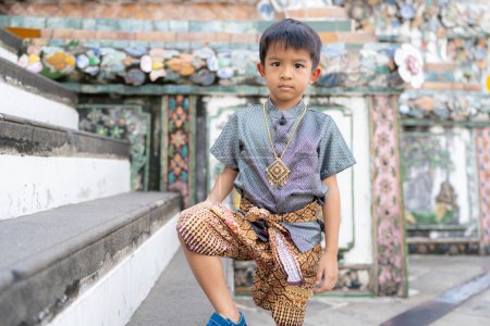Foto de Pequeño chico asiático llevar traje tradicional tailandés viajar en el templo del amanecer Wat arun Bangkok Tailandia - Imagen libre de derechos
