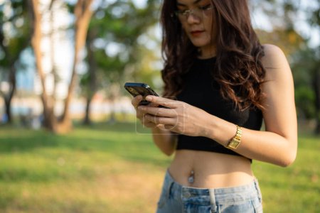 Téléchargez les photos : Business casual asiatique femme utiliser smartphone dans le parc de la ville coucher de soleil communication d'affaires en ligne - en image libre de droit