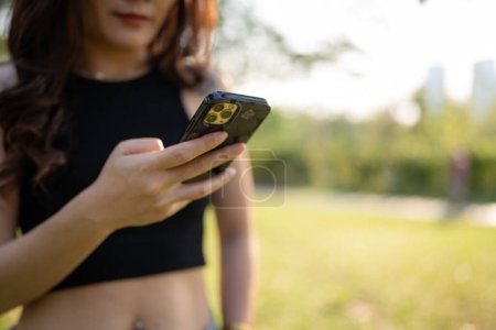Photo for Business casual asian woman use smartphone in city park sunset light online business communication - Royalty Free Image