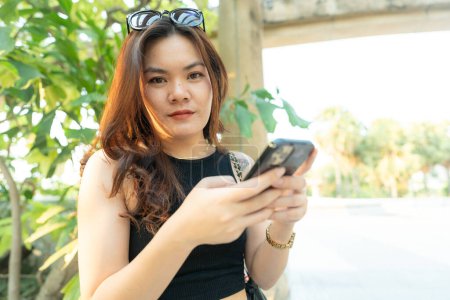 Téléchargez les photos : Business casual asiatique femme utiliser smartphone dans le parc de la ville coucher de soleil communication d'affaires en ligne - en image libre de droit