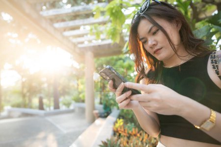 Business casual asiatique femme utiliser smartphone dans le parc de la ville coucher de soleil communication d'affaires en ligne