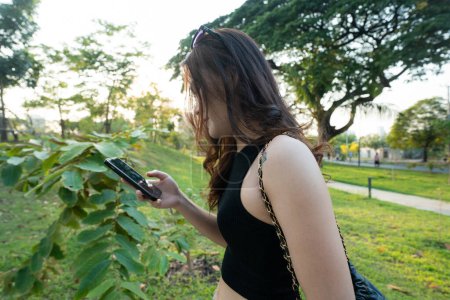 Business casual asian woman use smartphone in city park sunset light online business communication