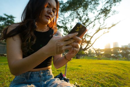 Business casual asian woman use smartphone in city park sunset light online business communication