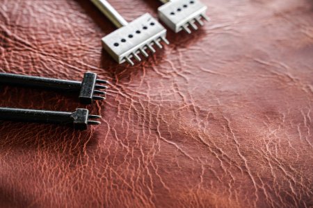 Téléchargez les photos : Outil de poinçonnage rond en métal pour le travail du cuir et bricolage sur fond de cuir - en image libre de droit