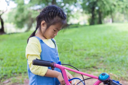 Photo for Asian kid girl ride bike in tree forest city public park outdoor exercise sunny day - Royalty Free Image