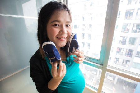 Téléchargez les photos : Heureux souriant pragmatique asiatique femme tenir bébé chaussure dans confortable chambre espoir nouveau-né concept - en image libre de droit