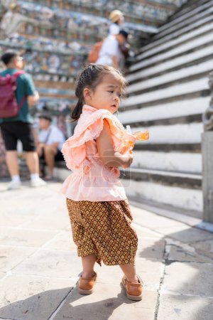 Photo for Toddler kindergarten girl wear Thai style costume travel in Wat Arun buddhist temple sightseeing travel in Bangkok Thailand - Royalty Free Image