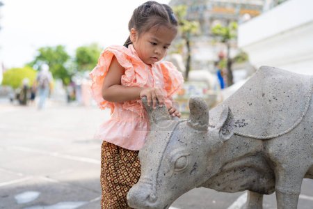 Toddler kindergarten girl wear Thai style costume travel in Wat Arun buddhist temple sightseeing travel in Bangkok Thailand