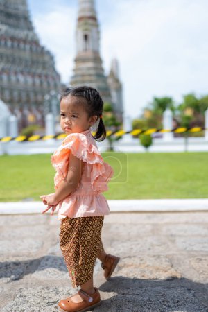 Téléchargez les photos : Enfant en bas âge fille de la maternelle porter Voyage costume de style thaïlandais à Wat Arun temple bouddhiste voyage touristique à Bangkok Thaïlande - en image libre de droit