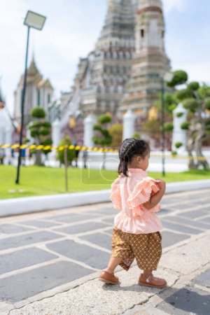 Toddler kindergarten girl wear Thai style costume travel in Wat Arun buddhist temple sightseeing travel in Bangkok Thailand