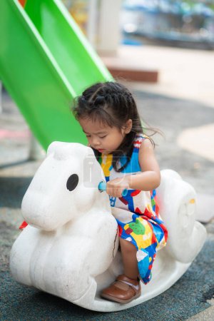 Photo for Adorable beautiful asian little girl playing outdoor playground Active kid on colorful slide and swing. Healthy summer activity - Royalty Free Image