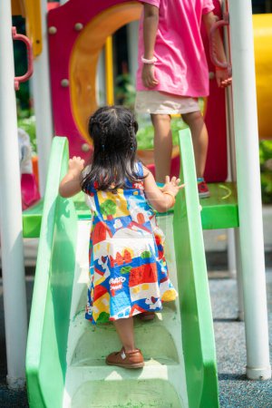 Téléchargez les photos : Adorable belle petite fille asiatique jouant terrain de jeu en plein air enfant actif sur toboggan coloré et swing. Activité estivale saine - en image libre de droit