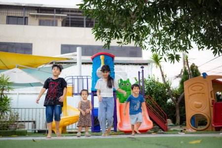 Téléchargez les photos : Petit asiatique garçon et fille enfants ami groupe courir ensemble dans enfant aire de jeux ville parc coucher de soleil lumière heureux temps - en image libre de droit
