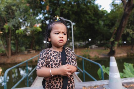 Téléchargez les photos : Petite fille asiatique se détendre dans le parc de la ville coucher de soleil lumière vert arbre insouciant loisirs de plein air - en image libre de droit