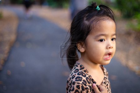 Photo for Little asian girl relax in city park sunset light green tree carefree outdoor recreation - Royalty Free Image