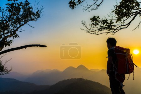 Foto de Senderismo hombre de pie en la colina disfrutando de la puesta del sol, Silhouette foto con mochila - Imagen libre de derechos