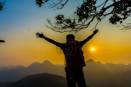 Téléchargez les photos : Homme de randonnée debout sur la colline profitant du coucher du soleil, Silhouette photo avec sac à dos - en image libre de droit