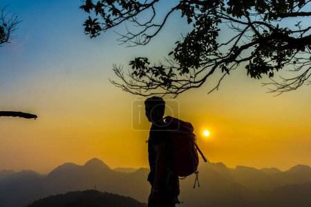 Foto de Senderismo hombre de pie en la colina disfrutando de la puesta del sol, Silhouette foto con mochila - Imagen libre de derechos