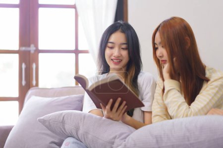 Téléchargez les photos : Activité à la maison concept, LGBT couple lesbien lit et apprendre la bible sainte ensemble dans le salon. - en image libre de droit