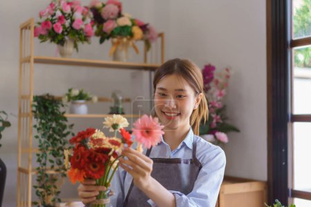 Téléchargez les photos : Concept floristique, Fleuriste femme arrangé gerberas colorées dans un vase en verre pour le client à la boutique de fleurs. - en image libre de droit