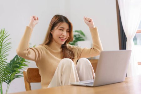 Téléchargez les photos : Travail du concept de la maison, Jeune femme asiatique lever les bras après avoir de bonnes nouvelles et de travailler avec succès. - en image libre de droit