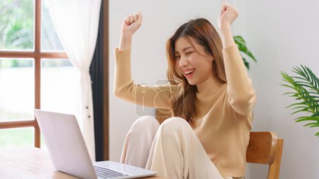 Téléchargez les photos : Travail du concept de la maison, Jeune femme asiatique lever les bras après avoir de bonnes nouvelles et de travailler avec succès. - en image libre de droit