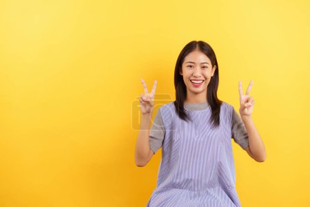 Téléchargez les photos : Jeunes femmes faisant signe v avec les deux mains et sourire avec un espace vide sur fond jaune isolé. - en image libre de droit
