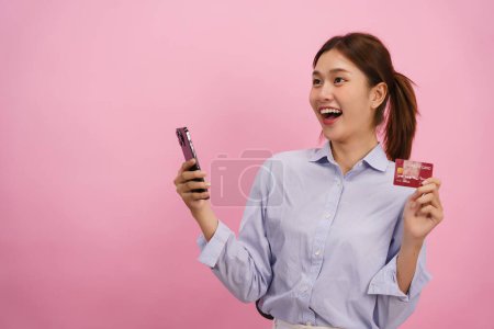 Téléchargez les photos : Femme tenant téléphone et carte de crédit pour faire du shopping en ligne avec un espace vide sur fond rose isolé. - en image libre de droit