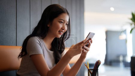 Téléchargez les photos : Asiatique adolescent femme étudiante en utilisant smartphone pour discuter avec des amis et surfer sur les médias sociaux après avoir étudié et lu des informations dans la paperasserie pour en apprendre davantage sur la connaissance de l'éducation dans le café. - en image libre de droit